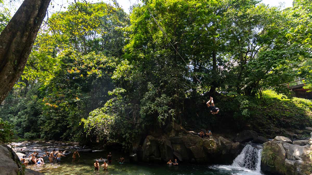 A man backflips from a rope swing above a river.