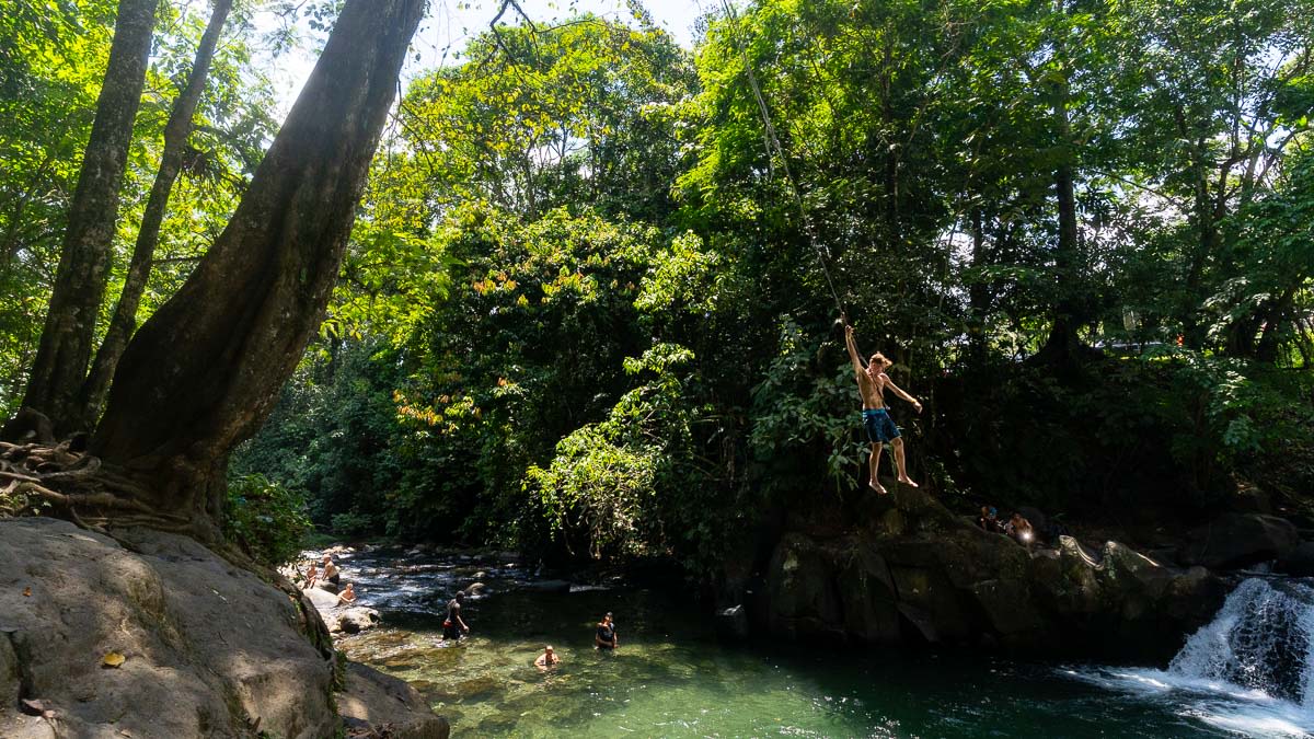 A man hangs from a rope swing above a river.