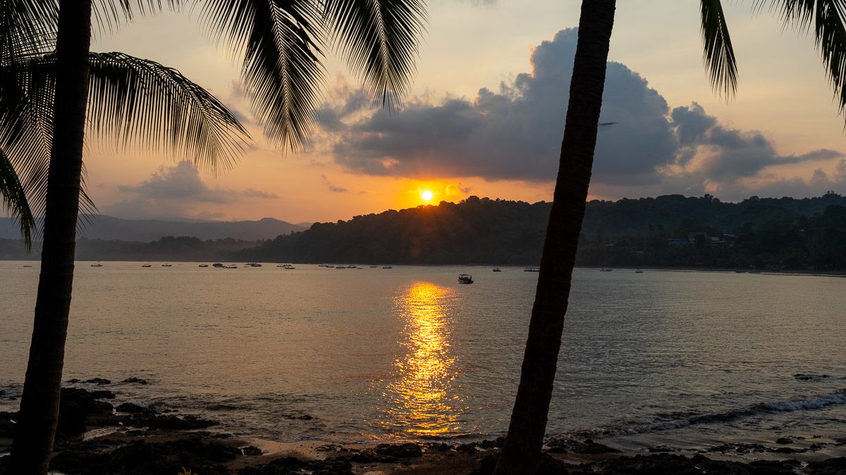 The sun rises over a small beach. The light illuminates small boats in the water.