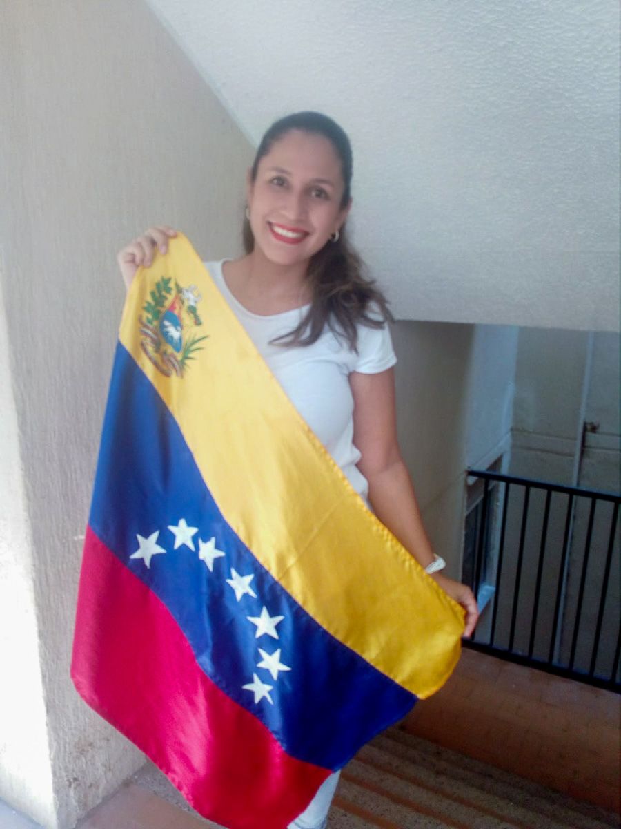 A woman smiles at the camera holding a Venezuela flag. 