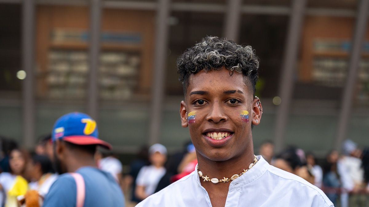 A young man smiles a the camera. He has a Venezuela flag painted on either cheek.