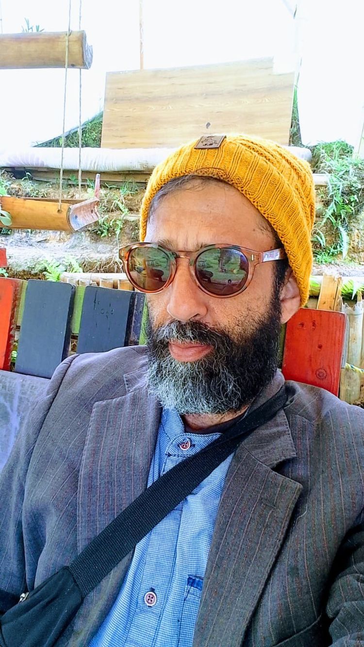 A man wearing a beanie hat and sunglasses looks at the camera. He has a beard.
