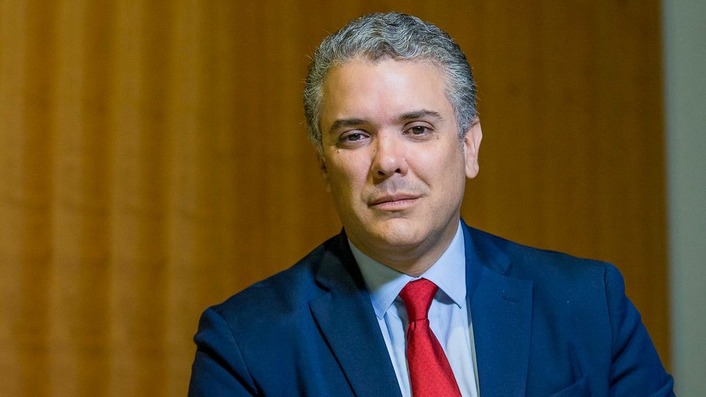 A man in a blue suit with a red tie looks at the camera.
